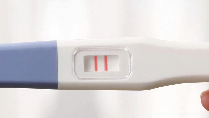 Mão feminina segurando um teste de gravidez positivo