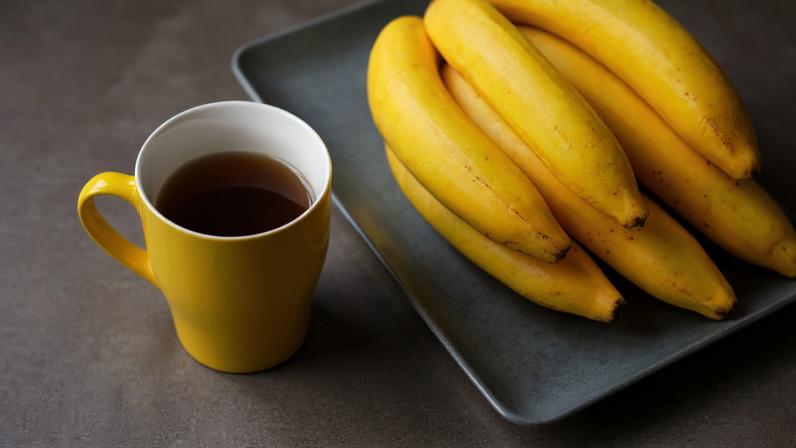 Cacho de banana ao lado de caneca amarela com chá dentro. Foto: Viktoriya | Adobe Stock