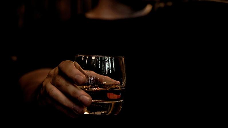Mão de pessoa segurando um copo de bebida de coloração como whisky
