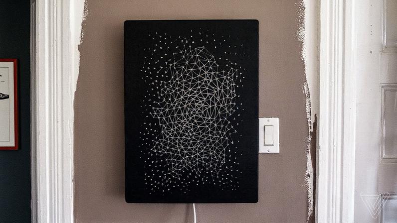 A black Ikea picture frame speaker with a geometric pattern design mounted on a wall beside a light switch.
