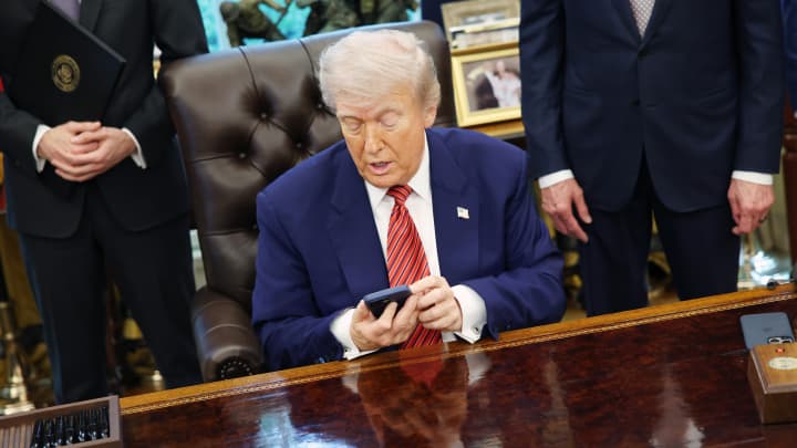 O presidente dos EUA, Donald Trump, segura um iPhone da Apple durante a assinatura de uma ordem executiva no Salão Oval da Casa Branca em Washington, DC, EUA, na sexta-feira, 23 de maio de 2025. (Foto: Samuel Corum | Bloomberg | Getty Images)