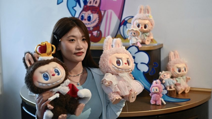 Mulher posando com os personagens Labubu (E) e Mokoko em um salão de exposições enquanto visita o parque temático Pop Land da Pop Mart, em Pequim (Foto: PEDRO PARDO / AFP)