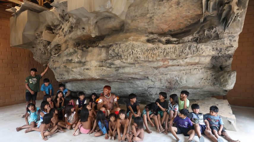 Cacique Akari Waurá cercado de crianças em frente à réplica da Gruta de Kamukuwaká (Foto: Alaor Filho/Fotos públicas)