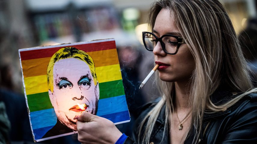 Mulher acende cigarro em cartaz representando o primeiro-ministro Viktor Orbán após o Parlamento húngaro aprovar uma lei que proíbe a comunidade LGBTQIA+ de realizar a marcha do orgulho (Foto: Marton Monus - 25.mar.2025/Reuters)