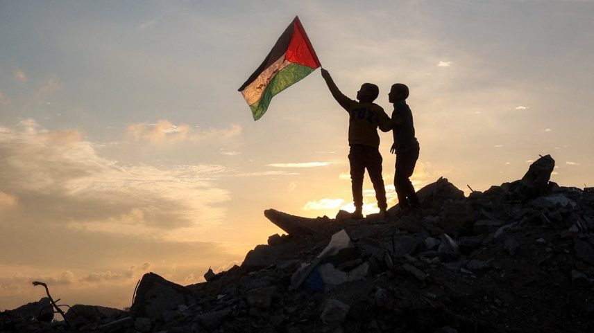 Um menino corre com uma bandeira palestina sobre um monte de escombros em um acampamento para pessoas deslocadas pelo conflito em Bureij, no centro da Faixa de Gaza (Foto: Eyad BABA / AFP)