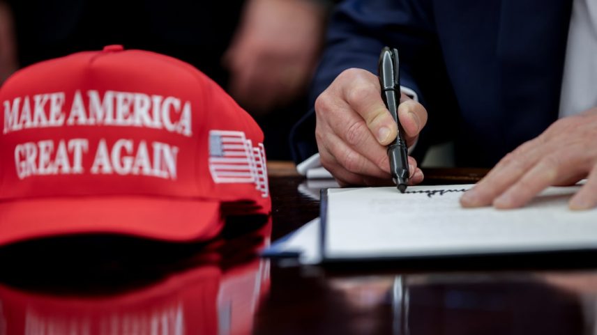 Donald Trump assina uma ordem executiva na Casa Branca ao lado do seu célebre boné escrito 'Make America Great Again' (Foto: Samuel Corum/Sipa/Bloomberg)
