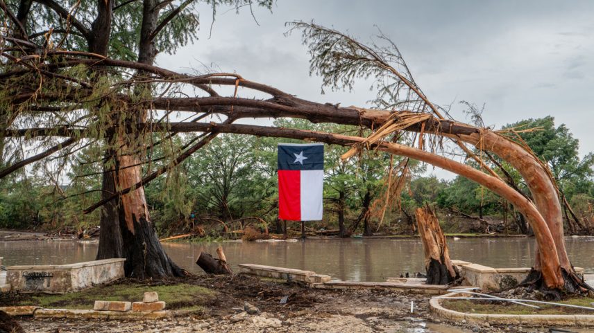 Uma bandeira do Texas pende de uma árvore danificada pela tempestade nas margens do rio Guadalupe em 13 de julho de 2025, em Center Point, Texas. (Foto: Brandon Bell/Getty Images)