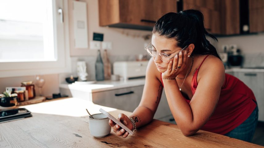 Uma mulher revisa seu smartphone na cozinha. (Foto: franckreporter/Getty Images)