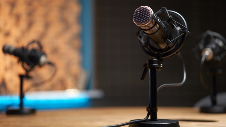 Microfone moderno em foco suave colocado sobre uma mesa de madeira em estúdio de gravação durante um podcast (Foto: Sergey Mironov/Getty Images)