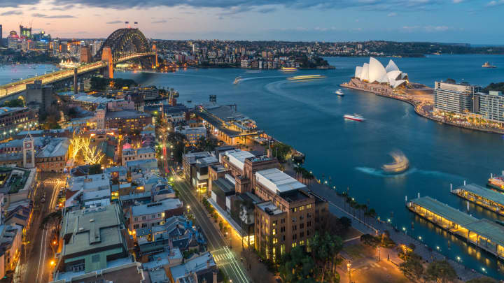 Cenário à beira-mar do centro da cidade de Sydney à noite, com a iluminação brilhante de marcos arquitetônicos modernos em Sydney, Austrália. (Foto: Prasit Photo | Moment | Getty Images)