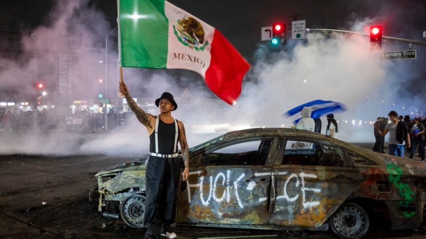 Manifestante segura bandeira do México em frente a pichação contra o Serviço de Imigração e Alfândega dos EUA (ICE, na sigla em inglês) em Los Angeles (Foto: RINGO CHIU / AFP)