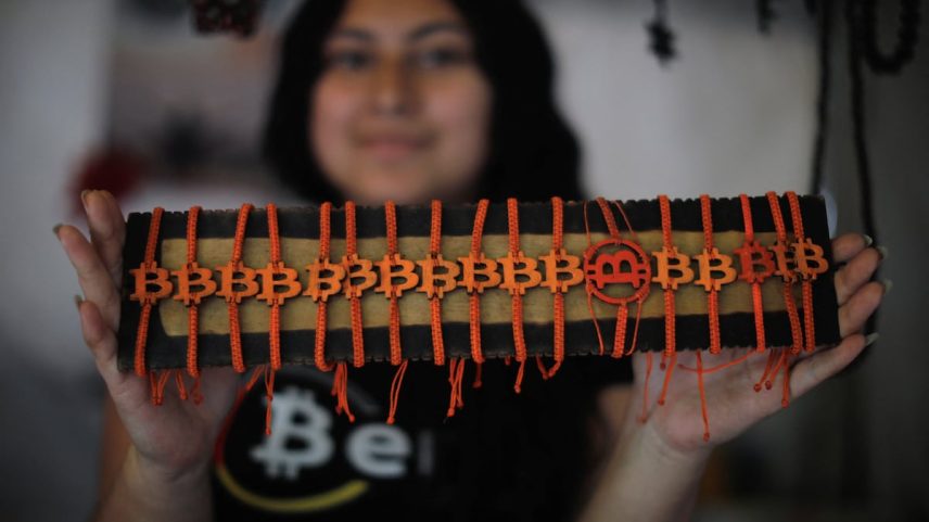 Uma mulher mostra brazaletes com temática de bitcoin à venda em Berlín, El Salvador, no dia 15 de julho de 2025. (Foto: José Cabezas/Reuters)