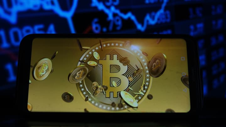 Logotipo do Bitcoin exibido em um smartphone com porcentagens do mercado de ações ao fundo. (Foto: Omar Marques | SOPA Images | LightRocket | Getty Images)