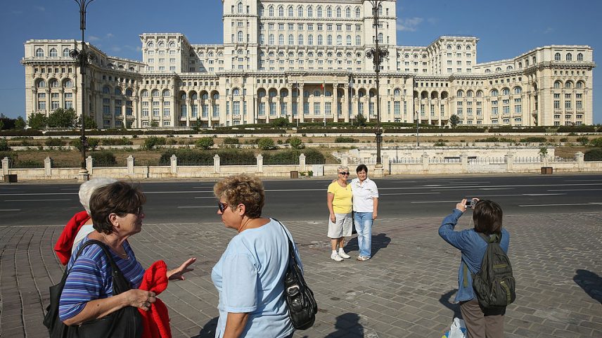 Turistas fotografam uns aos outros em frente ao Palácio do Parlamento em Bucareste, Romênia. O MNAC está localizado em uma ala dos fundos do edifício. (Foto: Getty Images)