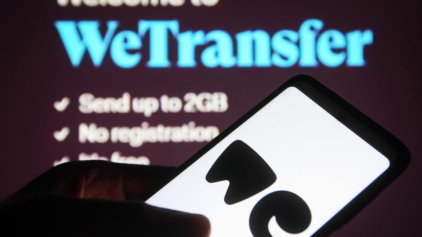 Um usuário maneja seu telefone frente a uma tela com o serviço WeTransfer aberto. (Foto: SOPA Images/SOPA Images/LightRocket via Getty Images)
