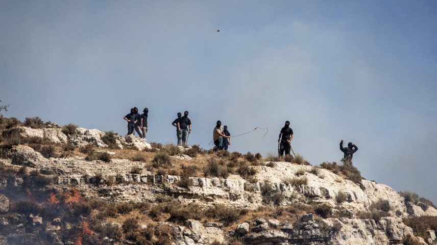 Colonos israelenses mascarados atiram pedras em palestinos do topo de uma colina na aldeia de Sinjil, na Cisjordânia ocupada, em 4 de julho (Foto: John Wessels/AFP)