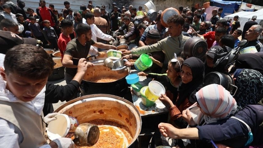 Palestinos fazem fila para receber uma porção de comida quente no campo de refugiados de Nuseirat, no centro da Faixa de Gaza (Foto: Eyad Baba / AFP)
