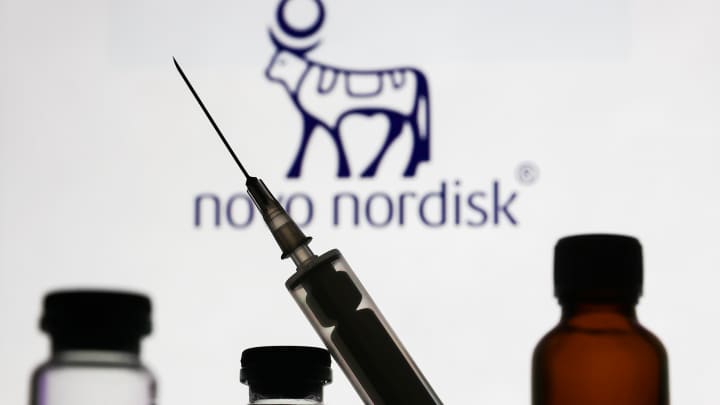 Frascos médicos e uma seringa são vistos com o logo da Novo Nordisk exibido em uma tela ao fundo. (Foto: Nurphoto | Nurphoto | Getty Images)