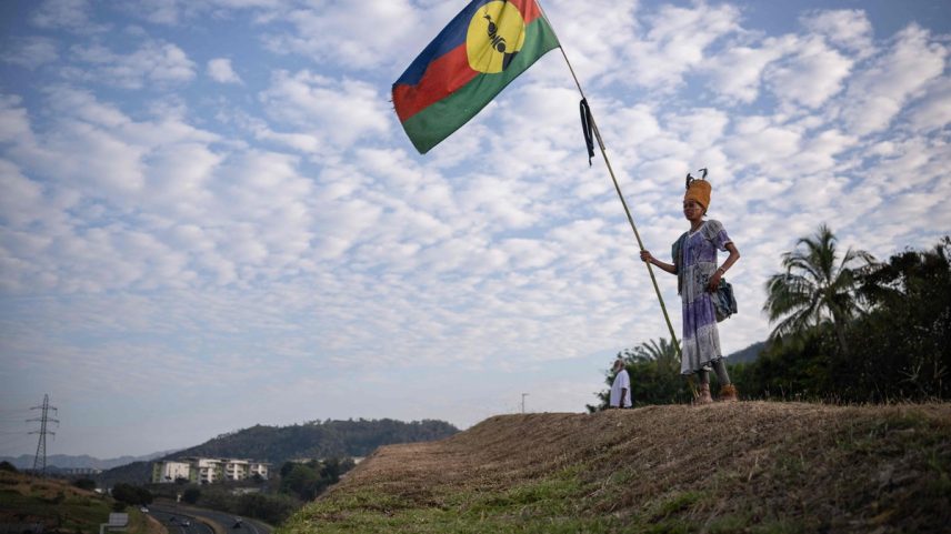 Mulher com vestido tradicional segura uma bandeira Kanak no distrito de Dumbea, em Noumea, no território francês do Pacífico da Nova Caledônia, em 24 de setembro de 2024 (Foto: Sebastien Bozon/AFP)
