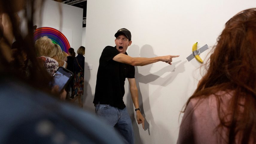 Um homem posa para uma foto ao lado de uma banana colada com fita adesiva que substitui a obra de arte ‘Comediante’ do artista Maurizio Cattelan, que foi comida por David Datuna, em Miami Beach, Flórida, 7 de dezembro de 2019. (Foto: REUTERS/Eva Marie Uzcategui/Foto de Arquivo)