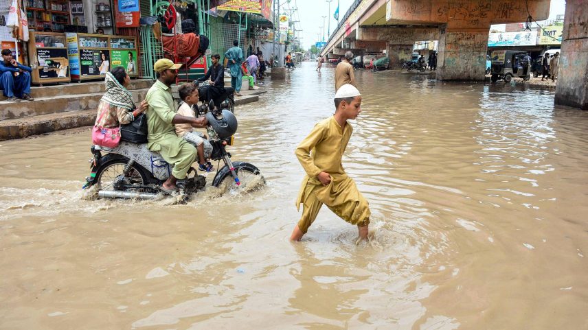 Pessoas atravessam uma rua alagada após fortes chuvas de monção em Hyderabad, na província de Sindh, no Paquistão (Foto: Akram Shahid - 20.jul.25/AFP)
