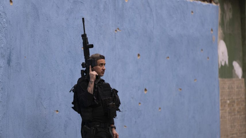 Policial armado diante de parede de escola em Parada de Lucas, no Rio, com marcas de bala (Foto: Márcia Foletto)