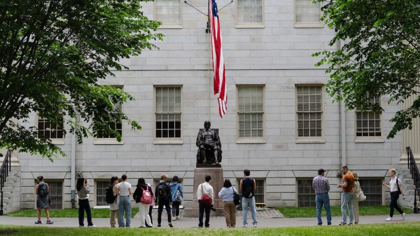 Alunos da Universidade de Harvard tiram fotos com a estátua de John Harvard, em Cambridge (Foto: Sophie Park /NYT)