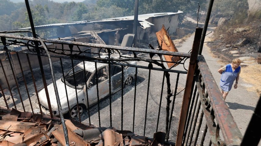 Uma mulher passava na quinta-feira frente a uma casa e um veículo queimados, em A Caridade (Ourense). (Foto: Lalo R. Villar (AP))