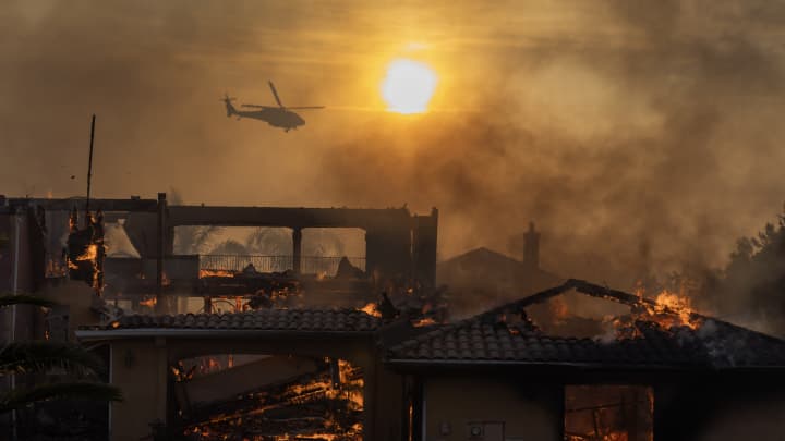 Um helicóptero de combate a incêndios voa perto de uma casa em chamas devido ao Incêndio da Montanha em 6 de novembro de 2024 em Camarillo, Califórnia. (Foto: David Mcnew | Getty Images News | Getty Images)