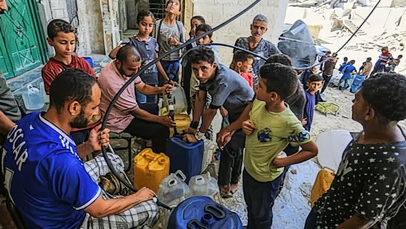 Palestinos recebem água potável da mezquita Al-Shafi e a levam para suas tendas, enquanto os contínuos bombardeios israelenses destruíram a infraestrutura do enclave, deixando os residentes sem acesso a água potável em Jan Yunis, Gaza, no dia 16 de agosto. (Foto: Reprodução)