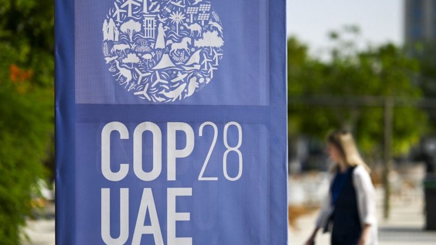 Uma mulher caminha perto de um painel com o logo da COP 28 exibido em Dubai. (Foto: Jewel SAMAD/AFP)