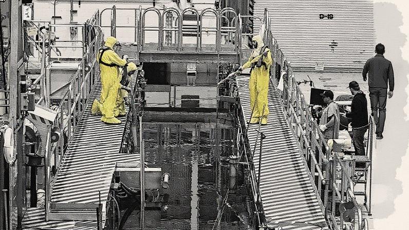 Trabalhadores em trajes de proteção estão em uma passarela acima de um líquido enquanto o combustível é carregado (Foto: Reprodução)