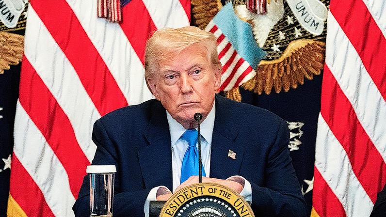 Homem em terno discute em um evento, com uma tela ao fundo mostrando um gráfico azul em ascensão (Foto: Reprodução)