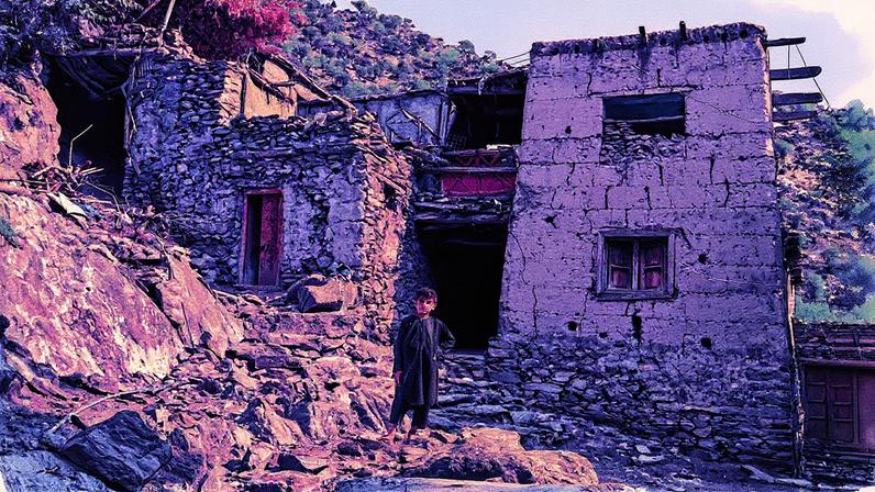 Menino em frente a casas danificadas por terremoto na vila de Masud, distrito de Nurgal, província de Kunar, Afeganistão (Foto: Reprodução)
