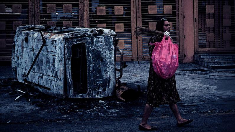 Mulher caminha com um saco de lixo perto de um veículo queimado durante o toque de recolher em Katmandu, Nepal (Foto: Reprodução)