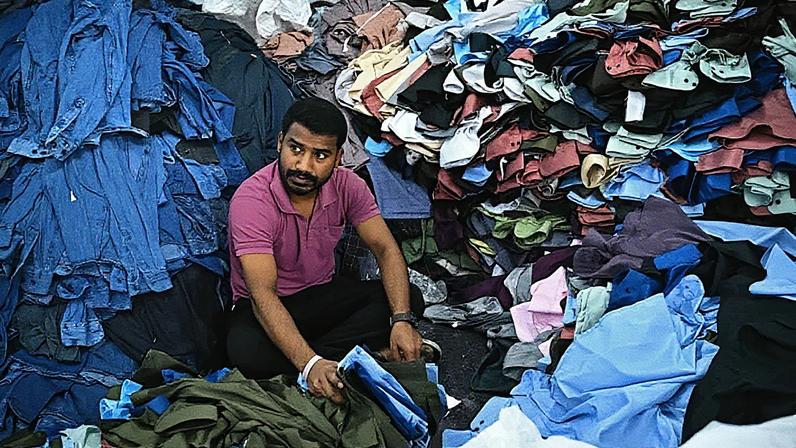Trabalhador de confecção organiza camisas sob medida e jeans em uma unidade de manufatura de vestuário em Bengaluru (Foto: Reprodução)