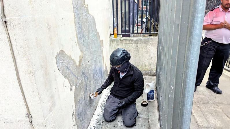 Trabalhador remove mural de Banksy que retratava um juiz agredindo um manifestante, localizado na parte externa do Tribunal Superior de Justiça de Londres (Foto: Reprodução)