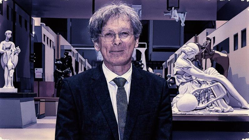 Homem em terno fala ao microfone durante apresentação em um palco com gráfico ao fundo (Foto: Reprodução)