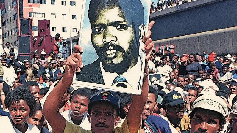 Homem em pé, com expressão séria, em um ambiente que remete à luta contra o apartheid na África do Sul (Foto: Reprodução)