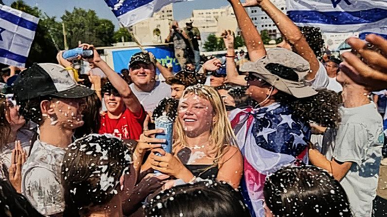 People wave Israeli flags and spray foam in celebration after the arrival of freed hostages.