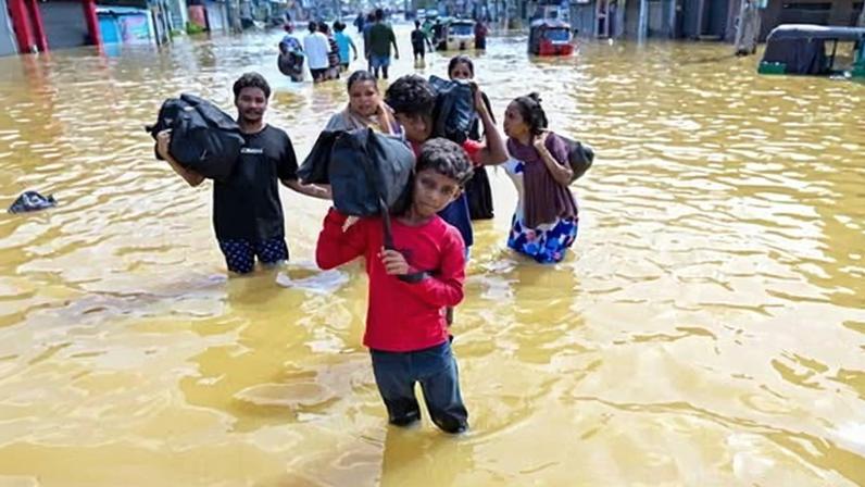 People wade through a flooded street with their belongings on Sunday after heavy rainfall in Wellampitiya, on the outskirts of Colombo.