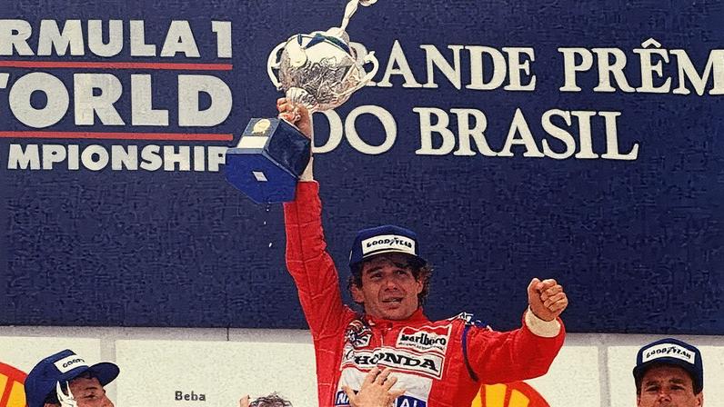 Exausto, Ayrton Senna ergue o troféu do GP Brasil de 1991. A vitória com câmbio travado é uma das mais emocionantes da história da F1. (Reprodução / Twitter)