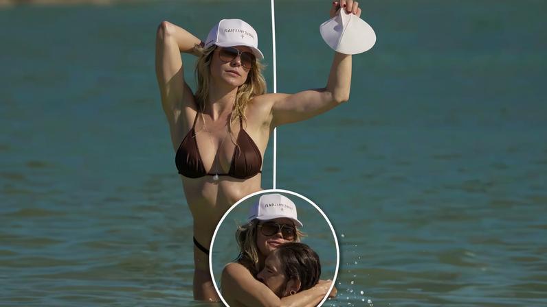Heidi Klum in a brown bikini and white cap, standing in the ocean.