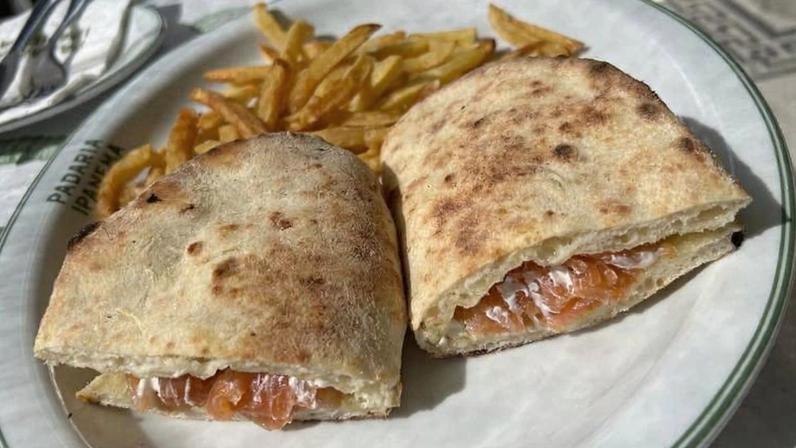 O sanduíche de salmão gravlax com cream cheese e alcaparras; o pão é uma massa de pizza assada na hora