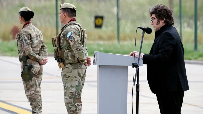 Javier Milei photographed at a military ceremony at a podium and microphone on an aircraft runway with two soldiers in the background