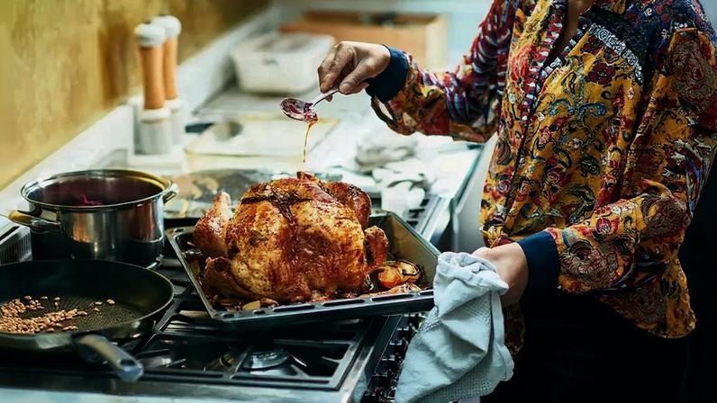 Fotografia de uma mulher segurando uma colher e regando um frango assado com óleo, preparando a ceia de Natal, jantar de Natal em família, ocasião especial, comida caseira.