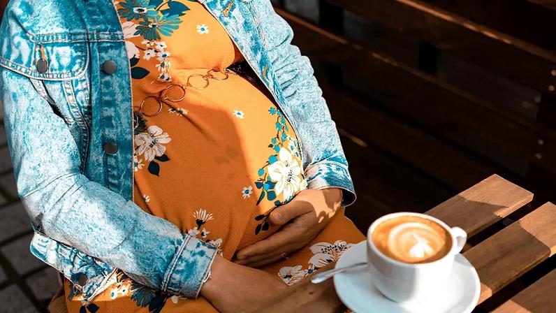 Fotografia de uma mulher grávida tomando uma xícara de café.