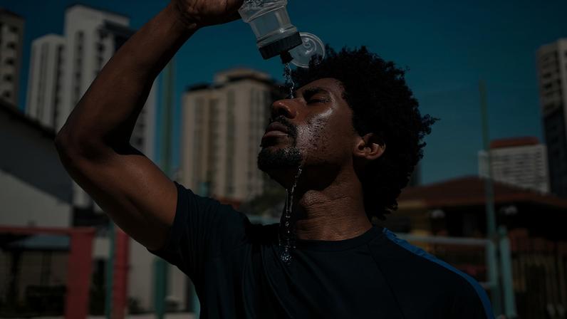 Fotografia de um homem negro despejando água na testa na por conta do calor.