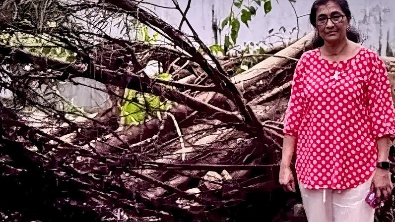 Contributed Irie Perera is wearing a red and white top, with white trousers. She has glasses on and is stood next to fallen trees.