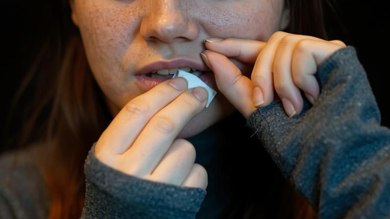 Teenager puts a sachet into her mouth, placing it under her upper lip